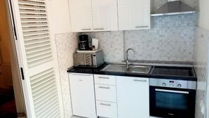 Una cocina compacta con armarios blancos, un horno Bosch, un microondas y un lavabo.