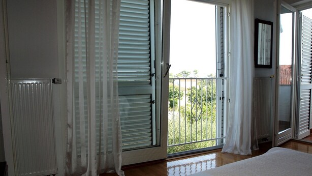 A bedroom with a large bed, sliding glass doors to a balcony, and a radiator.