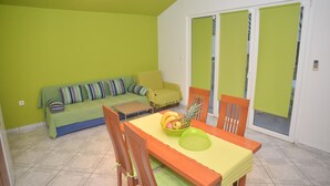 A dining area with a table set for two, a sofa, and a sliding glass door leading to an outdoor area. - Barić - Traditional One Bedroom Apartment with Balcony (A2) (Biograd na Moru)