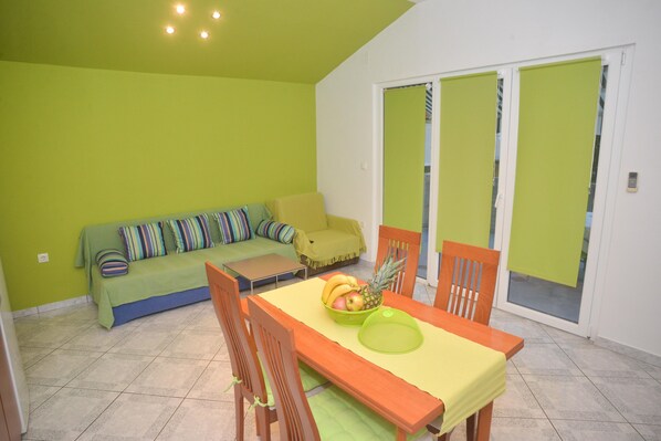 Un comedor con una mesa preparada para dos personas, un sofá y un ventanal corredero que da a un espacio exterior.