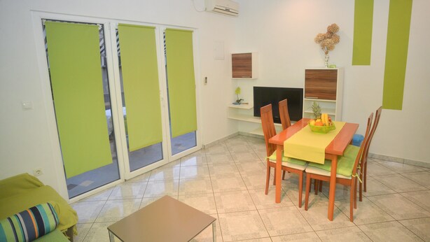 A dining area with a table set for two, a television on a stand, and a sliding glass door leading to an outdoor area. - Barić - Traditional One Bedroom Apartment with Balcony (A2) (Biograd na Moru)