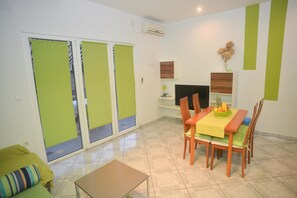 Un comedor con una mesa dispuesta para dos, un televisor sobre un mueble bajo y un ventanal corredero que da a un espacio exterior.