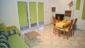 A living room with a green sofa, a small table, a dining table with chairs, and a TV on a wooden stand. - Barić - Traditional One Bedroom Apartment with Balcony (A2) (Biograd na Moru)