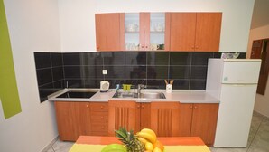 A kitchen with wooden cabinets, a white refrigerator, and a fruit bowl on the counter. - Barić - Traditional One Bedroom Apartment with Balcony (A2) (Biograd na Moru)
