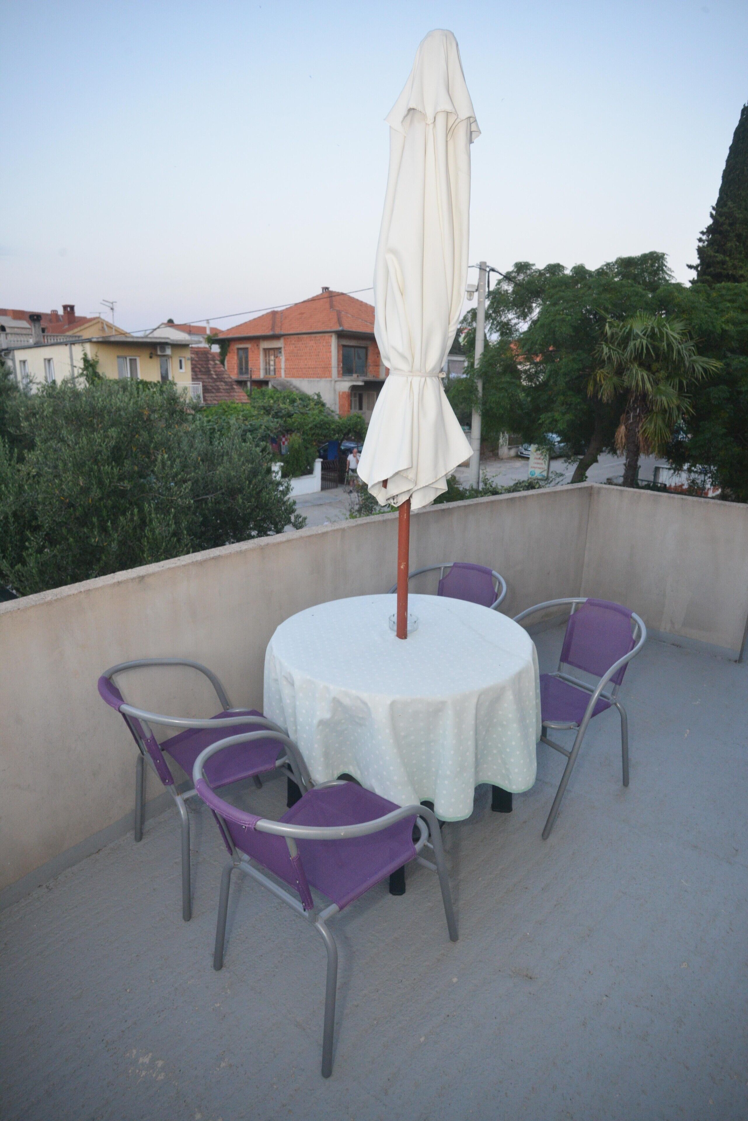Ein runder Tisch mit weißer Tischdecke und vier violetten Stühlen auf einer Dachterrasse.