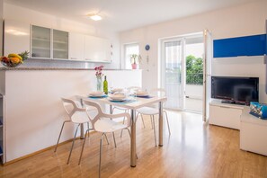 Una cocina moderna con armarios blancos, una mesa de comedor con sillas, un televisor y un balcón con una planta en maceta.