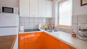 Eine Küche mit weißen Oberschränken, orangefarbenen Unterschränken, einer Mikrowelle, einer Kaffeemaschine und einem Fenster mit Jalousien.