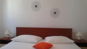 A neatly made bed with white and orange pillows, two wall art pieces, and a wooden headboard. - Katarina - Traditional Two Bedroom Apartment with Sea View (Razanac)
