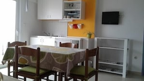 A dining area with a table set for four, surrounded by wooden chairs with green cushions. A white cabinet with shelves is visible in the background. - Katarina - Traditional Two Bedroom Apartment with Sea View (Razanac)