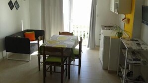 A compact living space with a dining table, chairs, a sofa, a small kitchen area, and a balcony with curtains. - Katarina - Traditional Two Bedroom Apartment with Sea View (Razanac)
