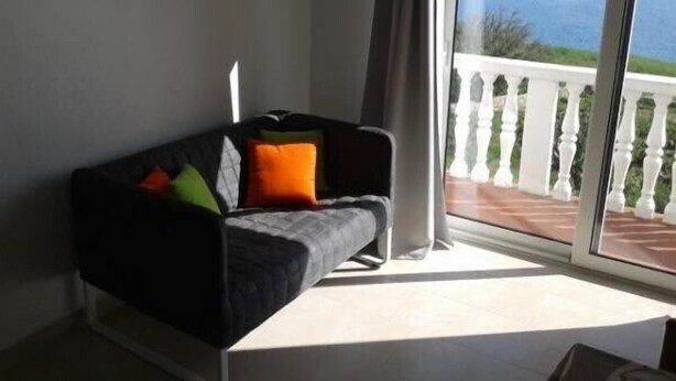 A room with a black sofa, a white railing, and a view of the sea. - Katarina - Traditional Two Bedroom Apartment with Sea View (Razanac)