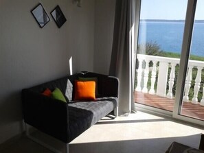 Een kamer met een zwarte bank, een witte balustrade en uitzicht op zee.