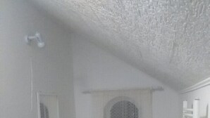 Une petite pièce, de taille modeste, avec un bureau blanc, un tabouret noir, une petite poubelle et un radiateur blanc.
