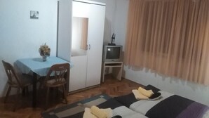 Una stanza piccola e arredata con un tavolo da pranzo, sedie, un divano, una televisione e un armadio.