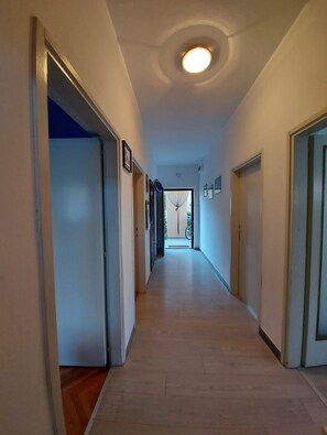 A hallway with wooden flooring, white walls, and a ceiling light.