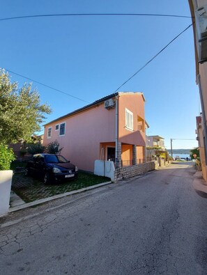 Un edificio de dos pisos con fachada rosa, base de piedra y un pequeño porche. Un coche negro está estacionado adelante.