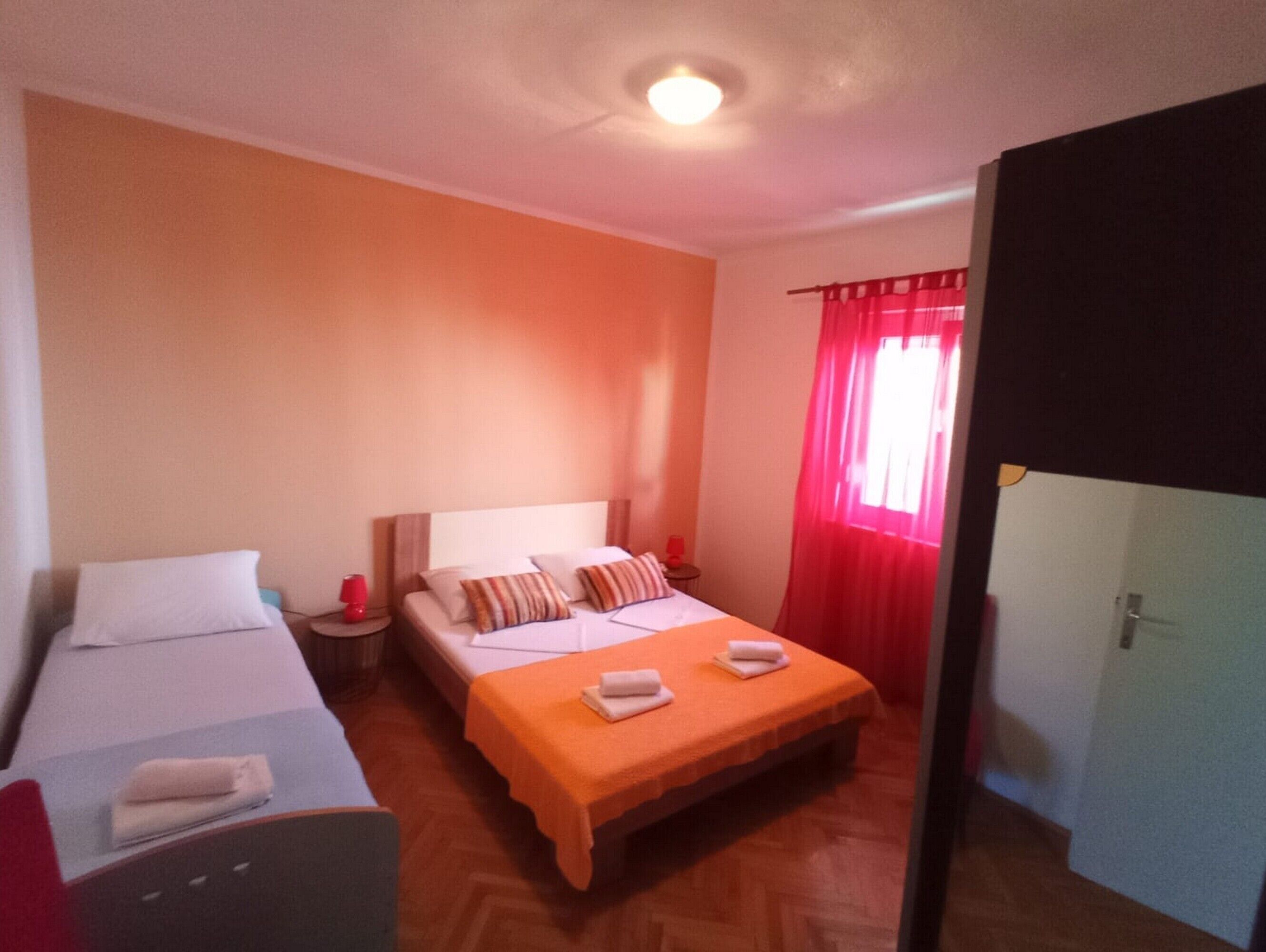 A hotel room with a bed, a sofa, a nightstand, and a window with red curtains.