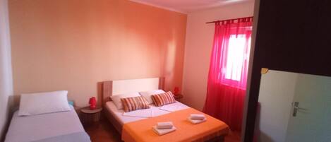 A hotel room with a bed, a sofa, a nightstand, and a window with red curtains.