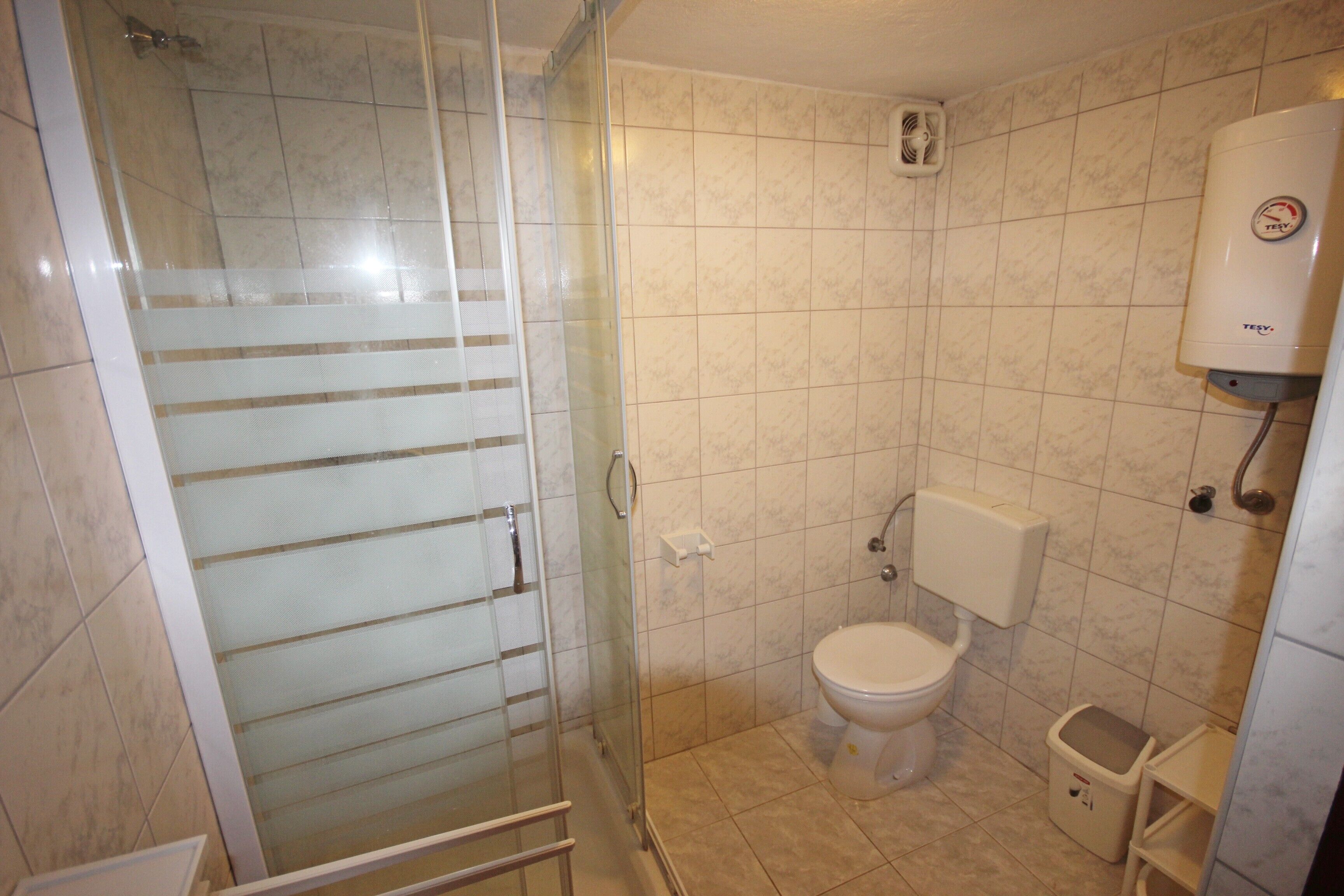 A bathroom with a glass shower enclosure, a toilet, and a white water heater.