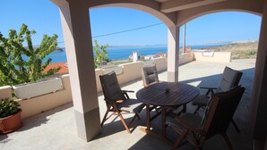 A covered outdoor seating area with a table and chairs, overlooking a scenic view of the sea and distant land. - Njaco - Two Bedroom Apartment with Terrace and Sea View (Razanac)