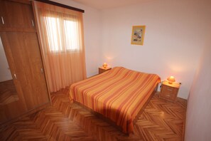 Ein Schlafzimmer mit gestreifter Bettdecke, Holzboden, einem Kleiderschrank, zwei Nachttischen mit Lampen und einem gerahmten Bild an der Wand.