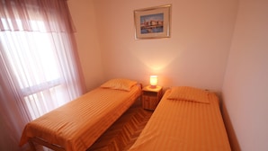 A room with two single beds, a nightstand with a lamp, a window with sheer curtains, and a framed picture on the wall. - Njaco - Two Bedroom Apartment with Terrace and Sea View (Razanac)