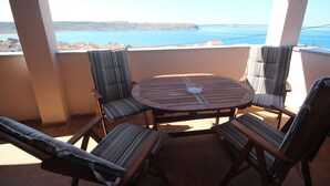 Ein runder Holztisch mit vier gestreiften Stühlen auf einem Balkon mit Blick auf ein Gewässer und die Ferne.