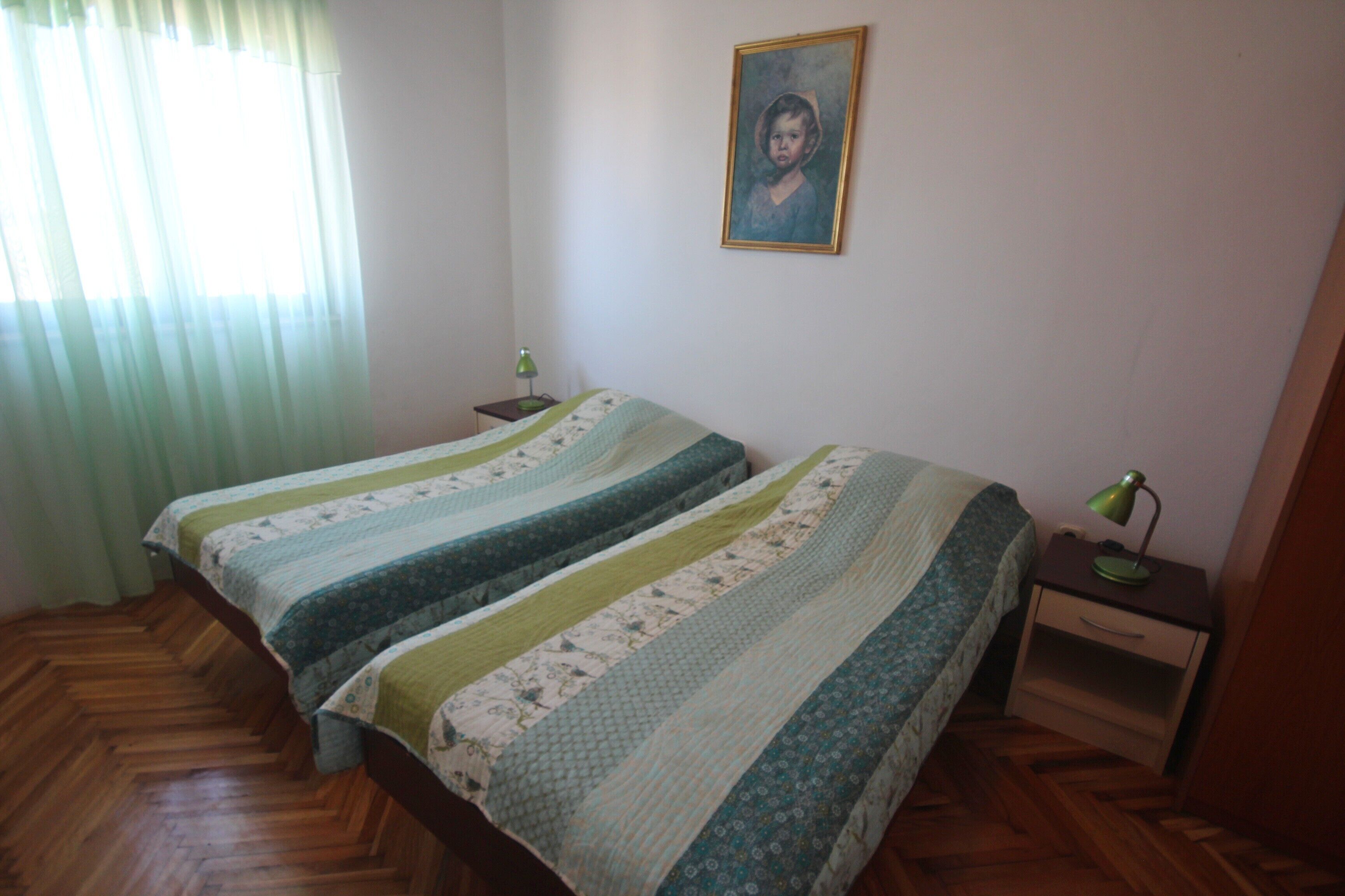 A room with two beds, a nightstand, a lamp, and a painting on the wall.