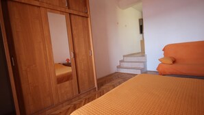 A bedroom with a wooden wardrobe, a bed with an orange bedspread, and a staircase leading to an upper floor.