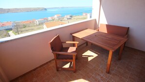 A balcony with a wooden table and chair, a view of the sea, and tiled flooring.