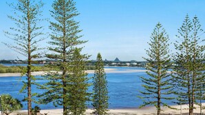 A coastal landscape with trees, a beach, and a distant cityscape. - Kookaburra Court U6 | Panoramic Ocean Views by Beach (Caloundra)