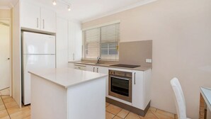 A modern kitchen with white cabinetry, a built-in oven, and a large island. - Kookaburra Court U6 | Panoramic Ocean Views by Beach (Caloundra)