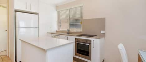 Een moderne keuken met witte kastjes, een inbouwoven en een groot eiland.
