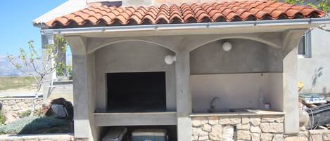 A stone-built outdoor kitchen with a tiled roof, a built-in sink, and a storage area.