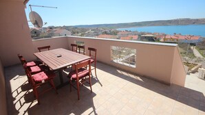 A balcony with a table and chairs, a satellite dish, and a view of a lake and buildings. - Njaco - Three Bedroom Apartment with Sea View (Razanac)