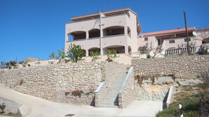 A multi-story building with a stone retaining wall, a staircase, and a clear blue sky. - Njaco - Three Bedroom Apartment with Sea View (Razanac)