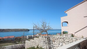 Un edificio costero con muro de piedra, vista despejada del mar y un edificio de techo rojo al fondo.