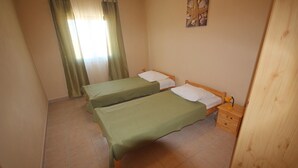 Una habitación con dos camas individuales, una mesita de noche de madera, una pequeña mesa y una ventana con cortinas.