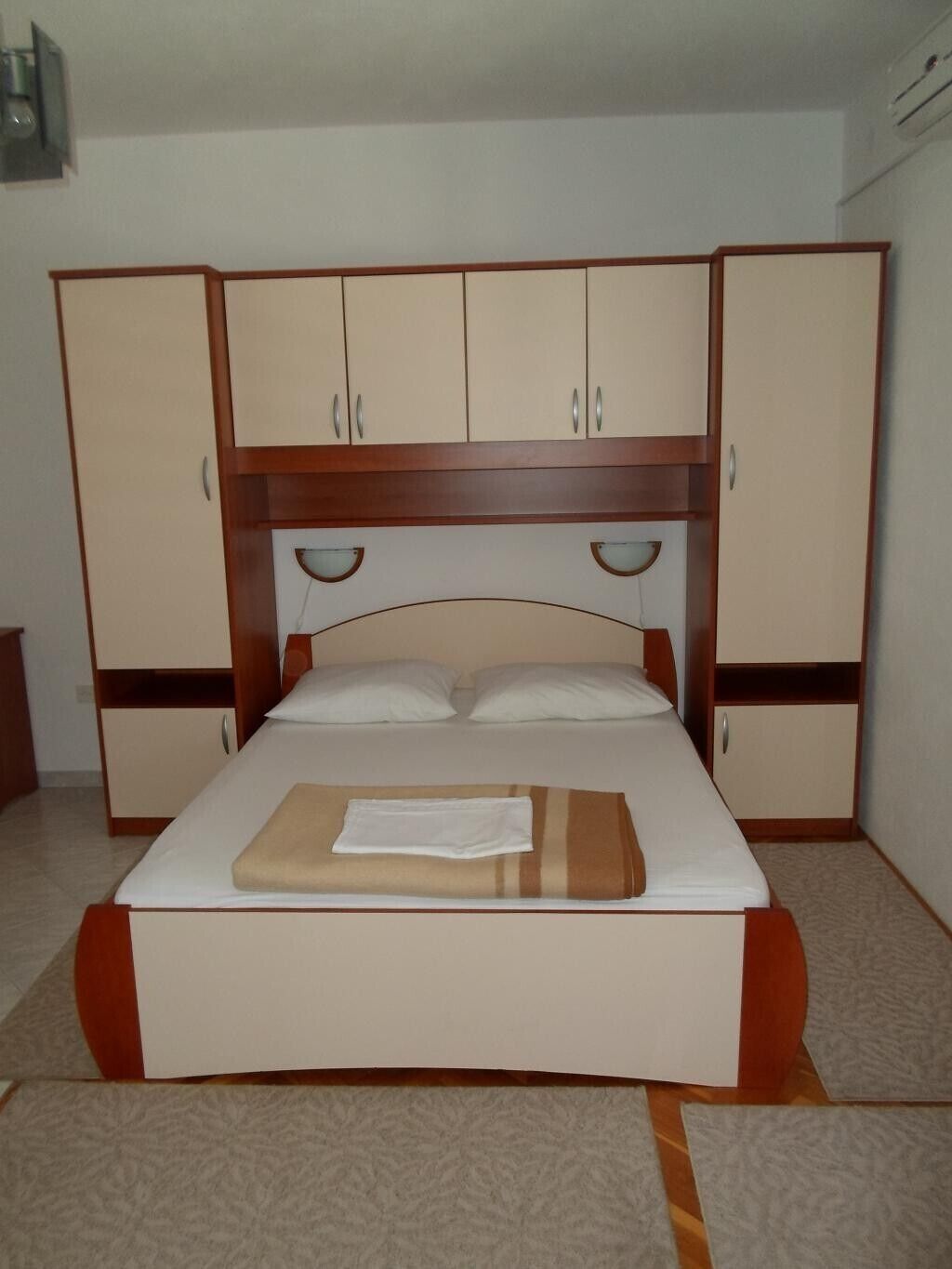 Un lit simple avec une tête de lit en bois, deux tables de chevet et une armoire à deux portes.