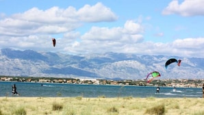A coastal area with mountains in the background, a beach, and people engaging in water activities. - Apartments Branko - Economy Studio Apartment with Balcony and Sea View (A4) (Nin)