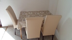 Et spisebord med et mønstret borddug, fire beige stole og et flisegulv.