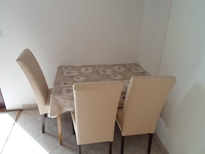 A dining table with a patterned tablecloth, four beige chairs, and a tiled floor.