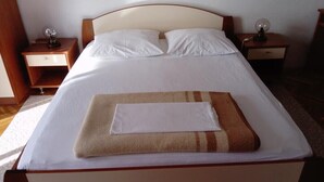 Ein ordentlich bezogenes Bett mit weißen Laken und einer braun-weißen Decke, zwei Nachttische mit Lampen und ein hölzernes Kopfende.