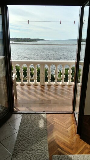 A view from a balcony with a wooden floor and white balustrade, overlooking a body of water and distant land.
