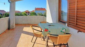 A balcony with a table and chairs, a window with wooden shutters, and a view of houses and greenery. - Apartments Suzana - Studio Apartment with Sea View (Bibinje)