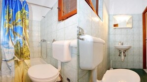Un baño con dos inodoros, una ducha, un lavamanos y un espejo.