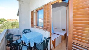 Un balcón con mesa y sillas, contraventanas de madera y vistas a edificios y zonas verdes.