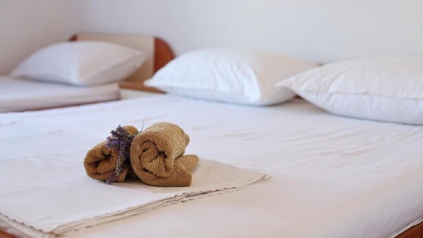 Una cama bien hecha con sábanas blancas y dos toallas enrolladas sobre la cama.