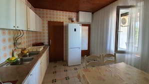 A compact kitchen with a refrigerator, wooden cabinets, a sink, and a dining table with chairs. - Apartment Rina- Two Bedroom Apartment with Terrace (Mandre)