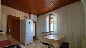 A compact kitchen with a refrigerator, a table with chairs, and a window with curtains. - Apartment Rina- Two Bedroom Apartment with Terrace (Mandre)